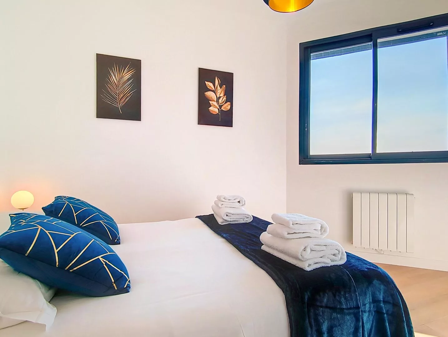 chambre ensoleillee cosy location appartement court sejour argenteuil Chambre lumineuse avec lit et coussins bleus.