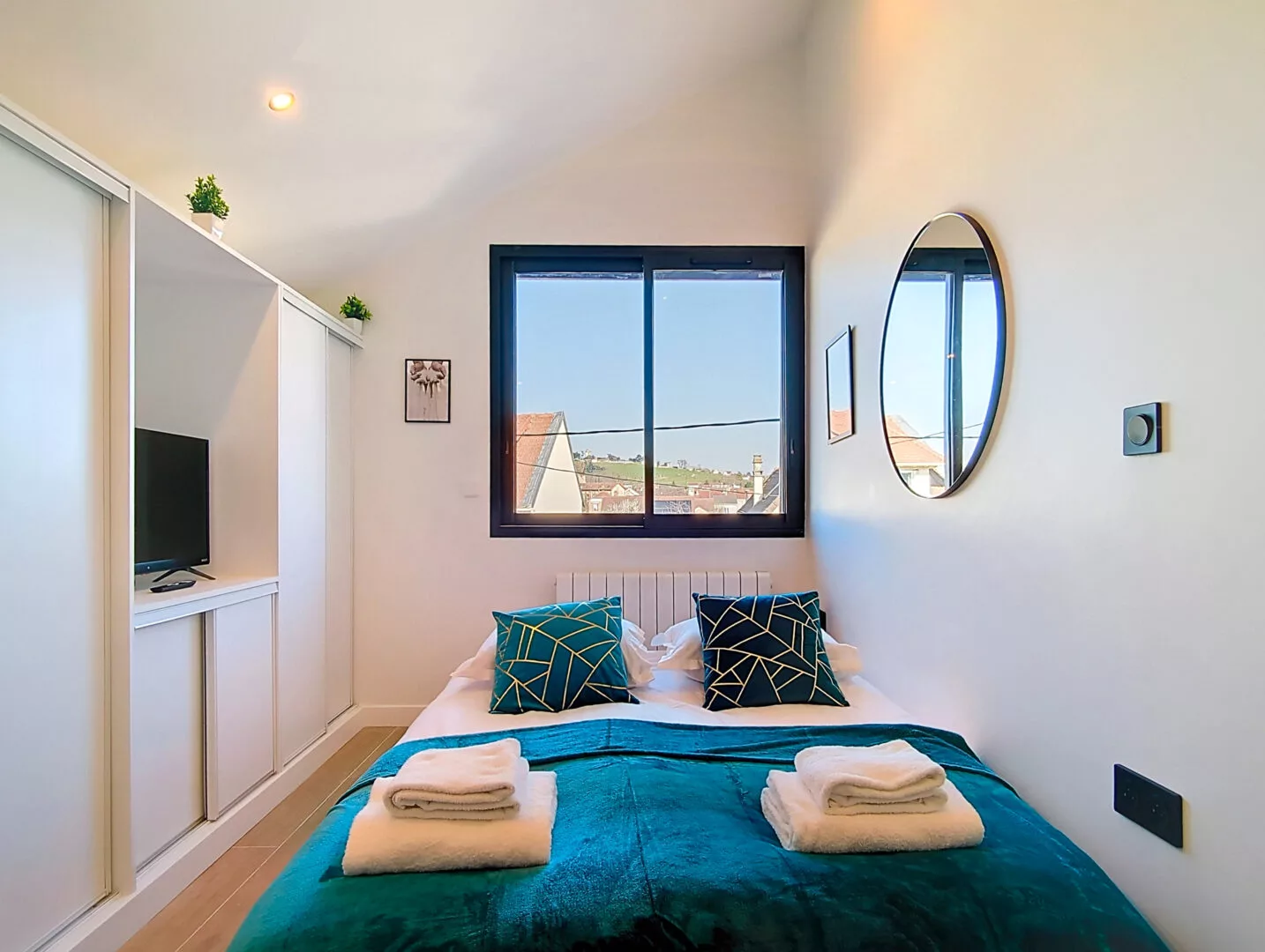 lit double et rangements location appartement court et long sejour argenteuil Chambre lumineuse avec lit, fenêtre et miroir rond.