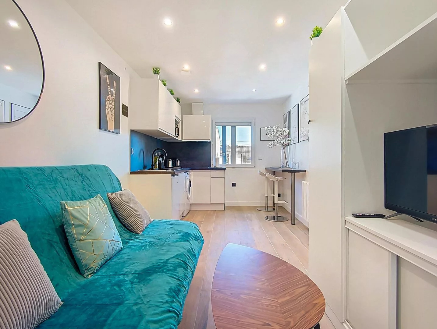 vue generale studio location appartement argenteuil Salon moderne avec canapé vert et cuisine intégrée.